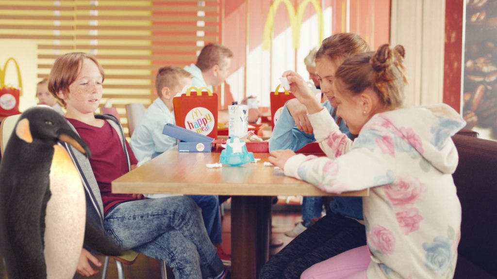 A group of kids sitting in a McDonalds restaurant playing with their happy meal toys next to our VFX-penguin.