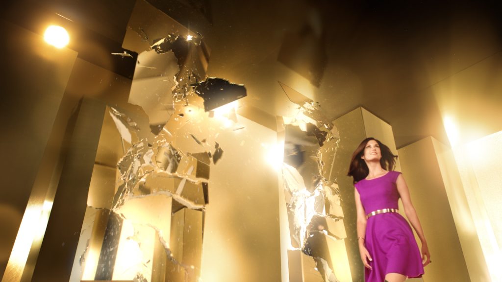 A woman in a purple wool dress walking through a bright golden VFX rendered room with lots of shattering mirrors.