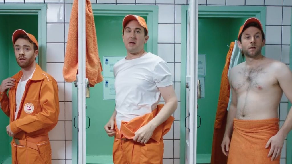 Three men in orange Zweifel "Cractive" overalls changing in front of green lockers.