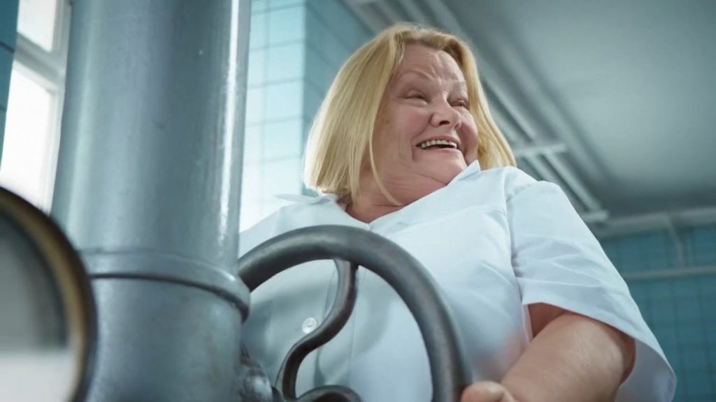 A stout, blonde nurse in white uniform is opening a big swivel valve.