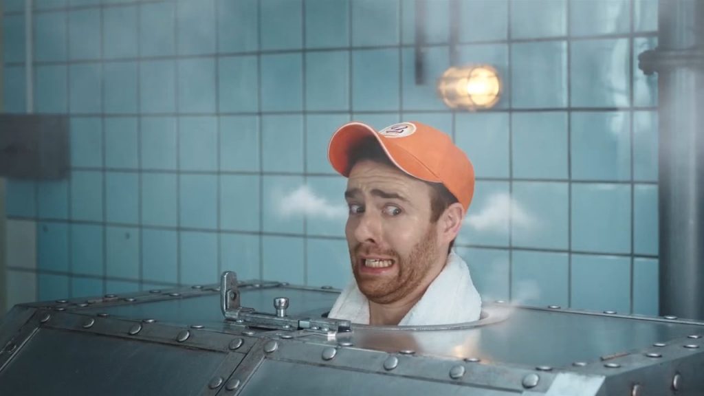 Another man wearing an orange Zweifel baseball cap in a russian metal-sauna with VFX-steam coming out of his ears.