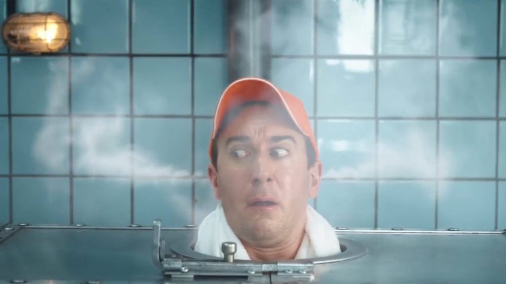 Another man wearing an orange Zweifel baseball cap in a russian metal-sauna with VFX-steam coming out of his ears.