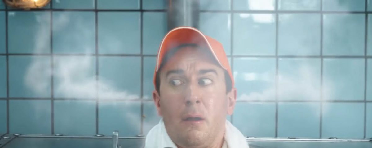 Another man wearing an orange Zweifel baseball cap in a russian metal-sauna with VFX-steam coming out of his ears.