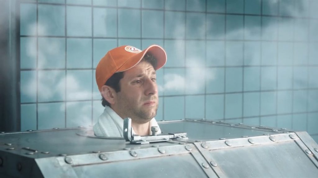 A man wearing an orange Zweifel "Cractive" baseball cap in a russian metal-sauna with VFX-steam coming out of his ears.